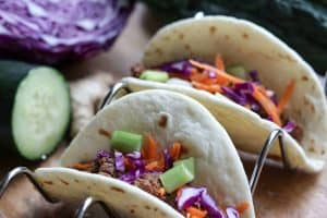 Quick, easy, healthy Korean Beef in the Instant Pot made into tacos on a taco rack with cucumber, red cabbage and ginger on a wooden board from Gourmet Done Skinny