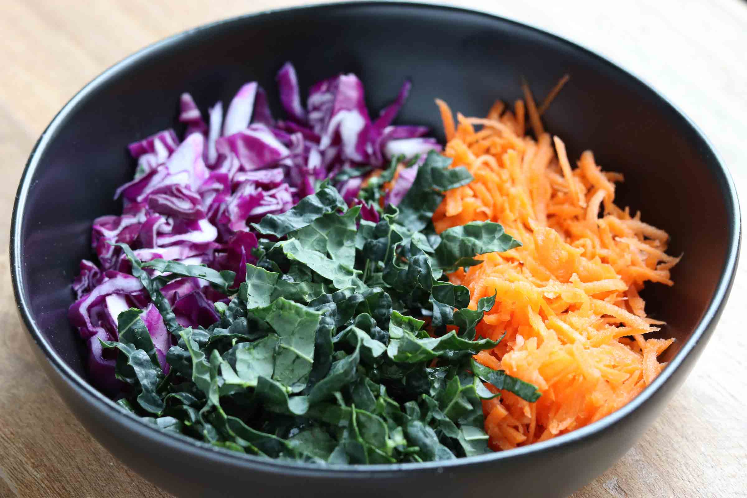 Kale, cabbage and shredded carrots in a black bowl on a wooden board from Gourmet Done Skinny