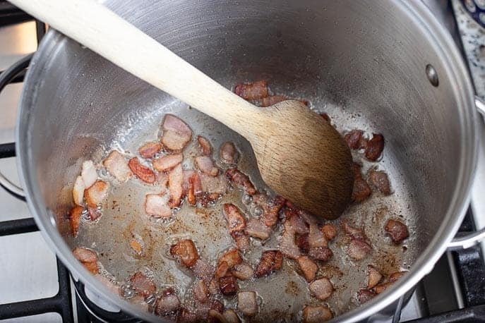 Small pieces of bacon frying in a pot with wooden spoon from Gourmet Done Skinny