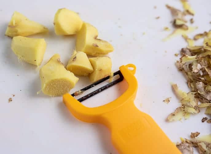Peeled ginger and peeler on a white cutting board