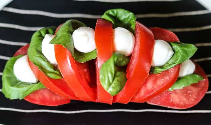 tomato sliced hasselback style on a black and white striped plate with basil, mozzarella and balsamic vinegar