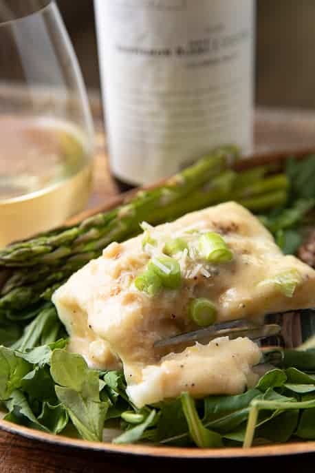 Air Fryer Halibut with Creamy Parmesan Sauce on a bed of arugula, white wine in a glass and bottle in background