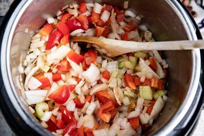 red peppers, onions, celery in an Instant Pot with wooden spoon
