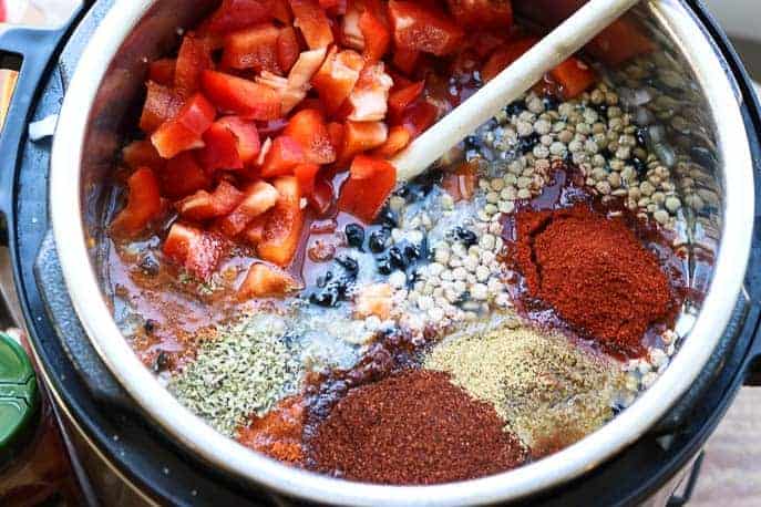 red peppers, lentils, black beans and spices in a Instant Pot with a wooden spoon