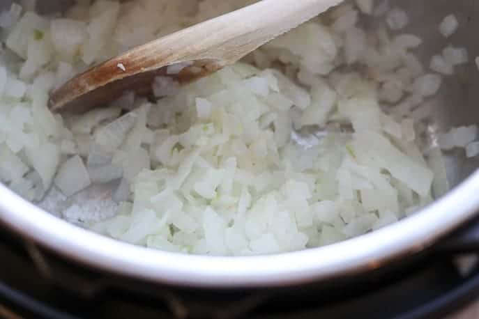 onions browning in an Instant Pot with a wooden spoon