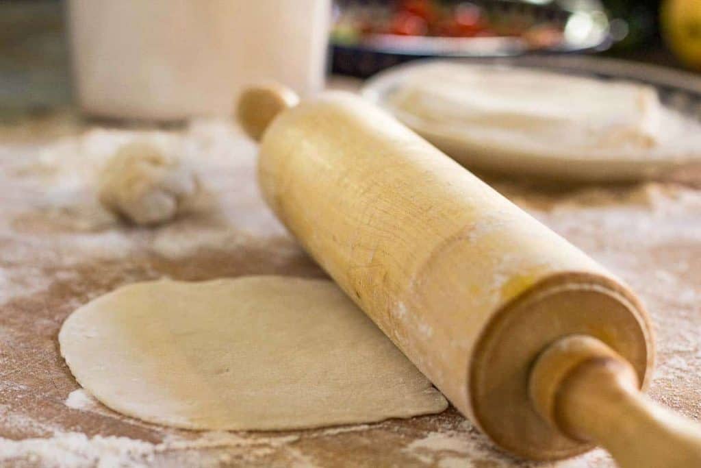 flour tortilla on a board with a wooden rolling pin
