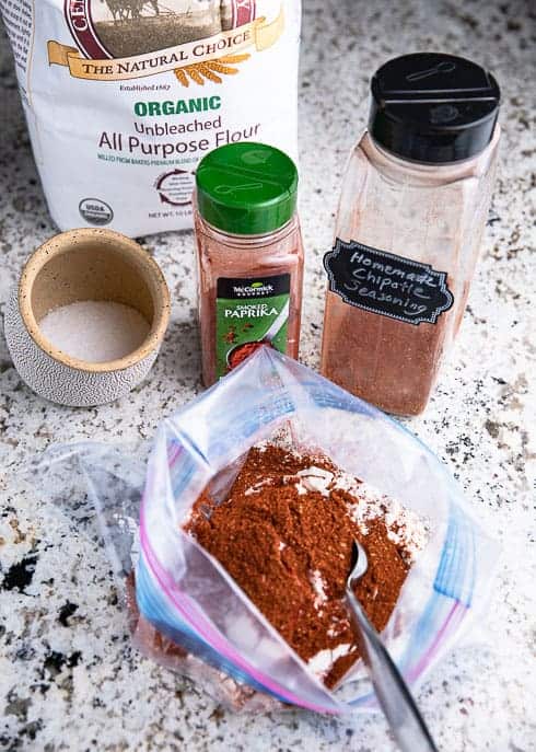 Ziplock bag with flour, homemade chipotle seasoning, salt, paprika and flour on a granite counter