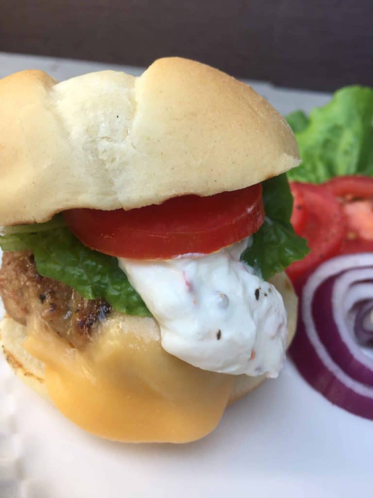 Turkey Slider with tomato and jalapeno cream, onions, lettuce in the background from Gourmet Done Skinny.
