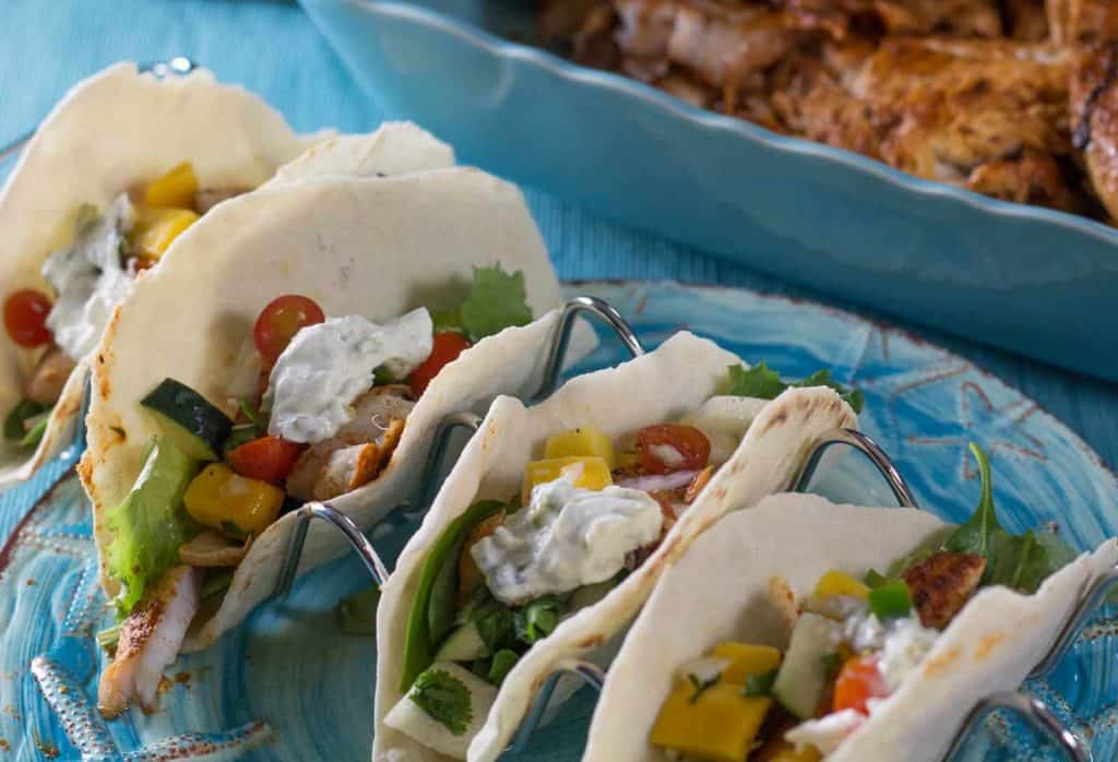 Rockfish tacos on a blue plate with a dish of fish in the background