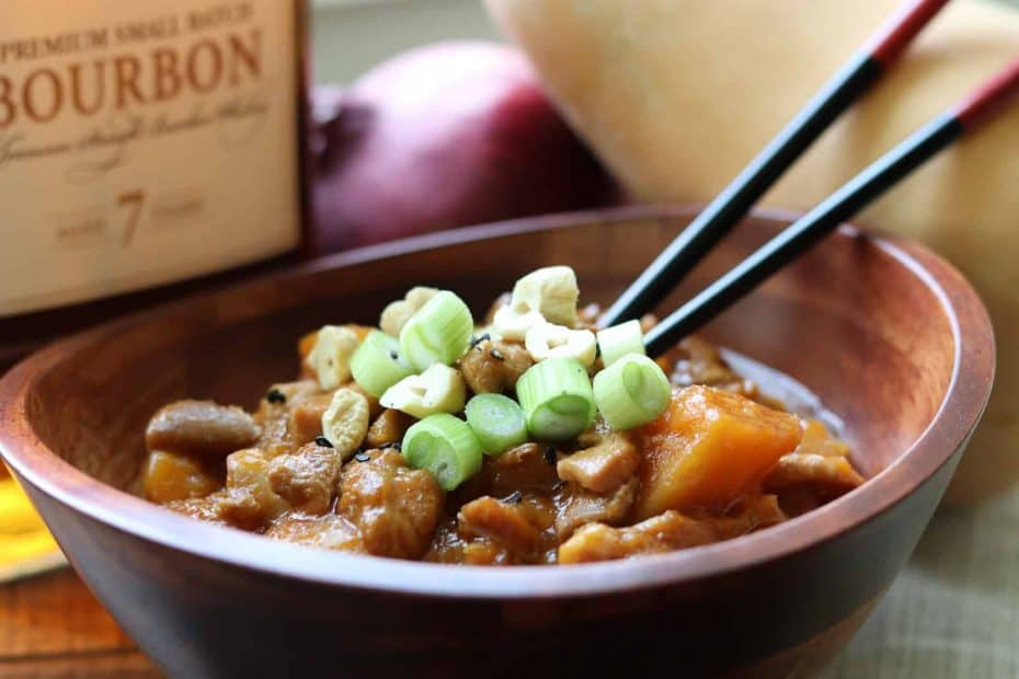 Instant Pot Bourbon Butternut Chicken from Gourmet Done Skinny in a wooden bowl with chopsticks, bourbon, butternut squash and onion on board nearby