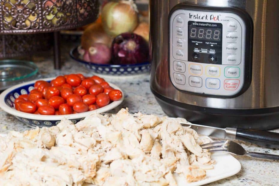 Instant Pot Shredded and Brined Chicken on a plate with Instant Pot and tomatoes and onions in background