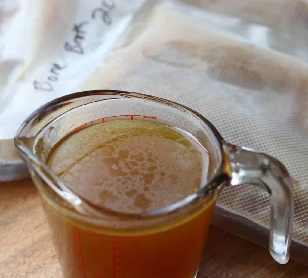 Healthy Instant Pot Beef Bone broth in a glass measuring cup and packages of bone broth in background