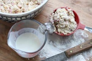 Bowl with scone dough, buttermilk in a liquid measuring cup and 1 cup of scone dough on a wooden board with knife, from Gourmet Done Skinny