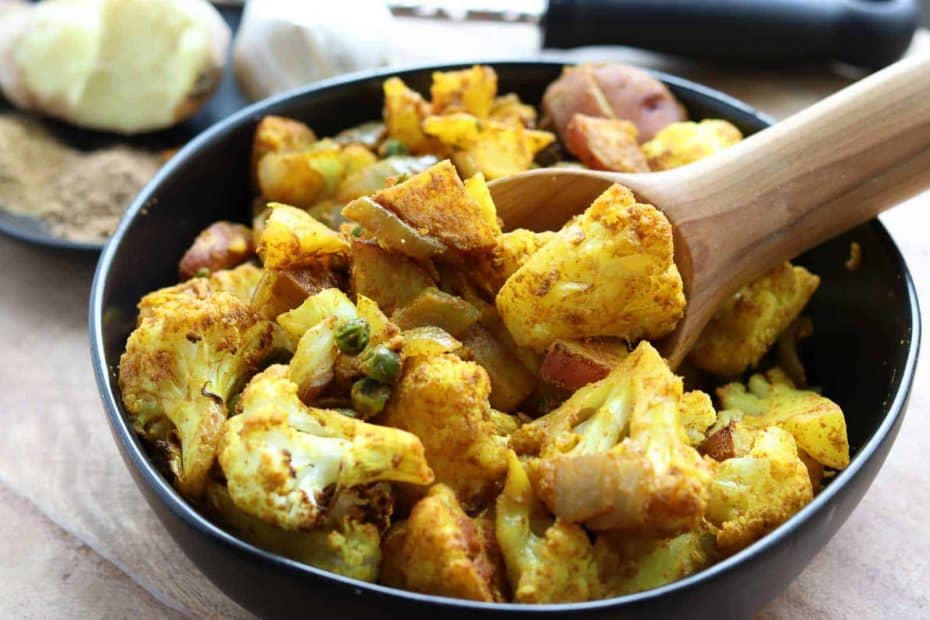 Roasted Indian Cauliflower Medley in a black bowl with wooden spoon from Gourmet Done Skinny
