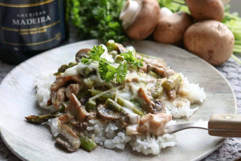 Easy Healthy Instant Pot Chicken Madeira on a wood plate with mushrooms, parsley and Madeira wine in the background from Gourmet Done Skinny