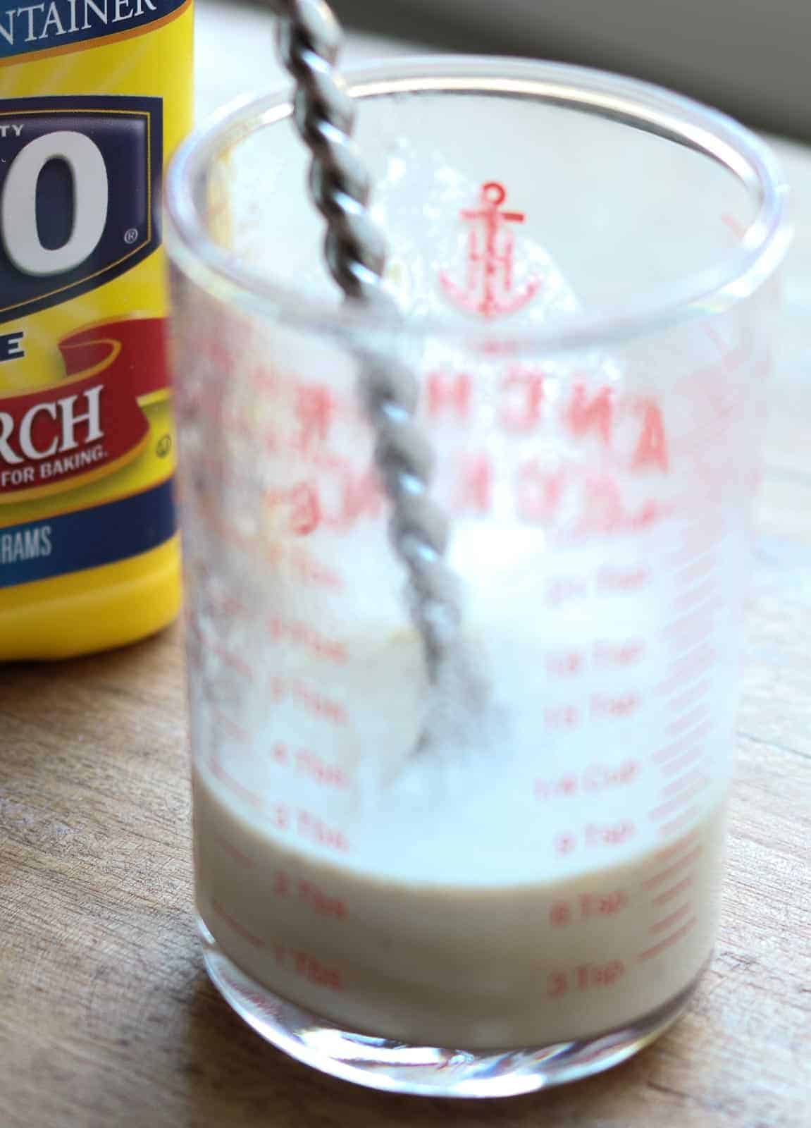 Liquid measuring cup with chicken liquid, cornstarch and spoon.