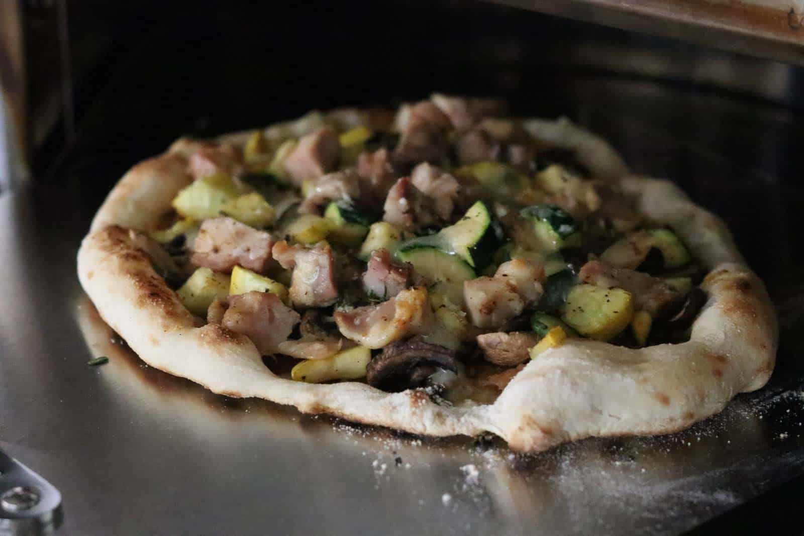 Healthy Wild Mushroom Pizza with Caramelized Onions, Garlic, Zucchini and Truffle Oil Pizza on a stainless steel pizza peel in oven