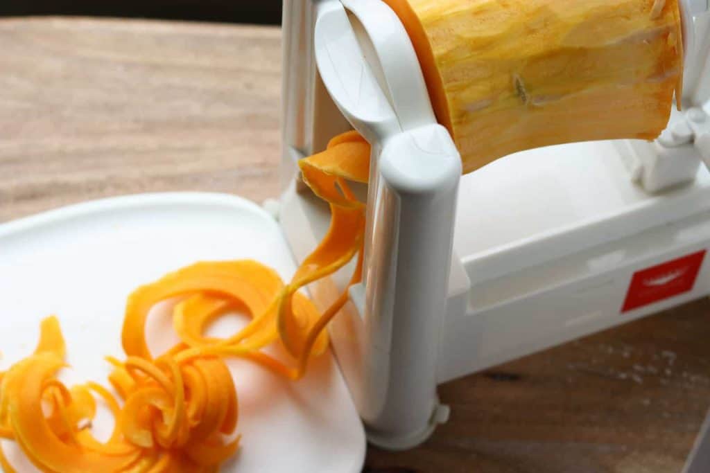 Butternut squash on a white cutting board with a Paderno spiralizer from Gourmet Done Skinny