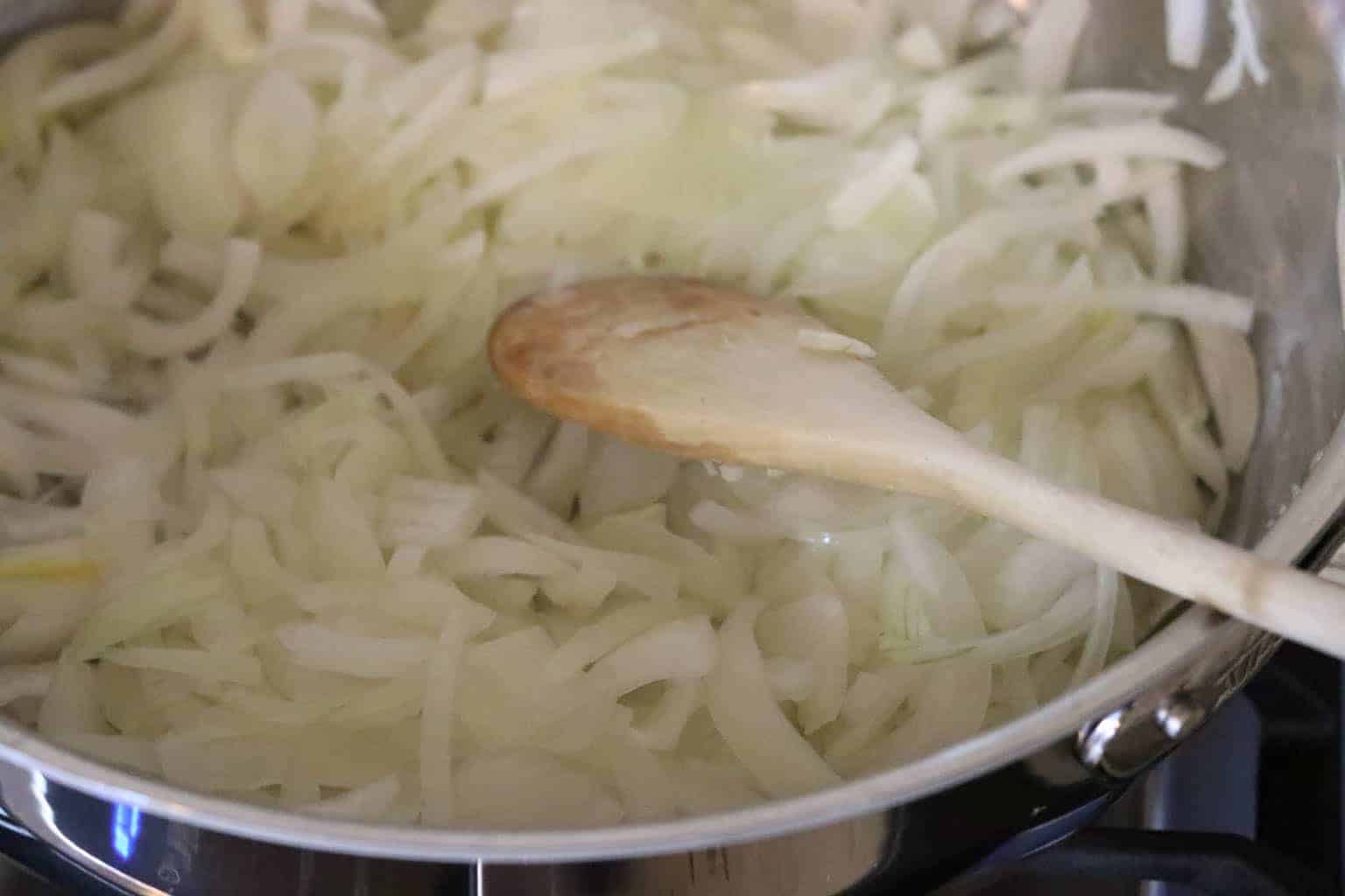Sliced onions in a metal pan with wooden spoon from Gourmet Done Skinny