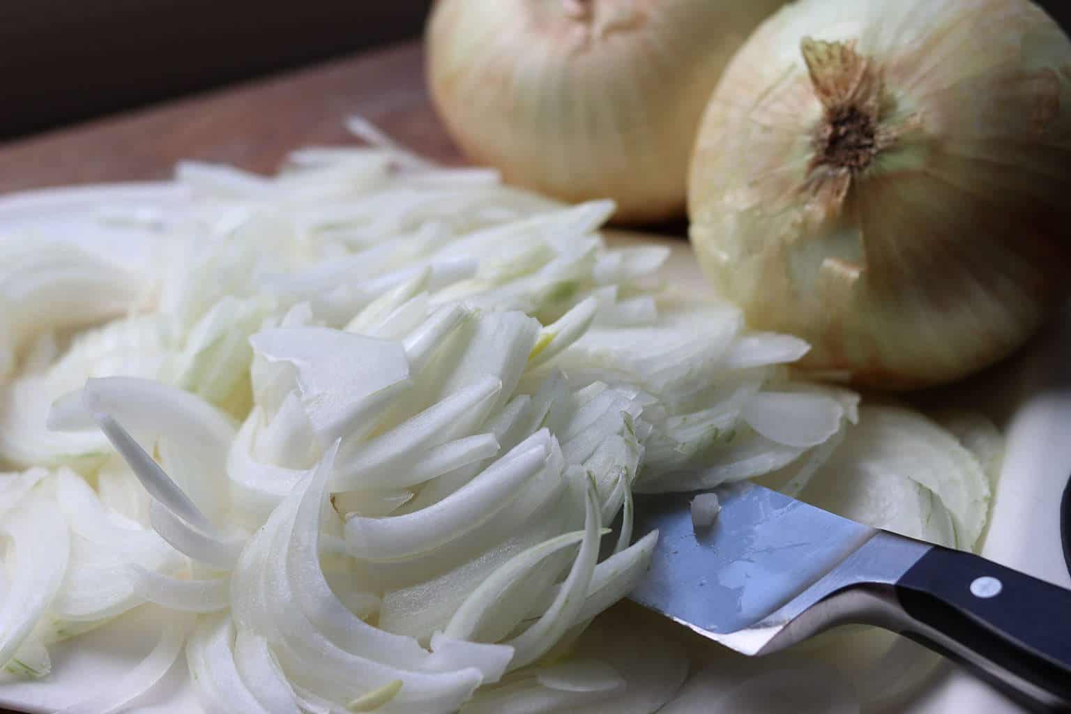Sweet onions sliced on a white cutting board with 2 onions in the background from Gourmet Done Skinny