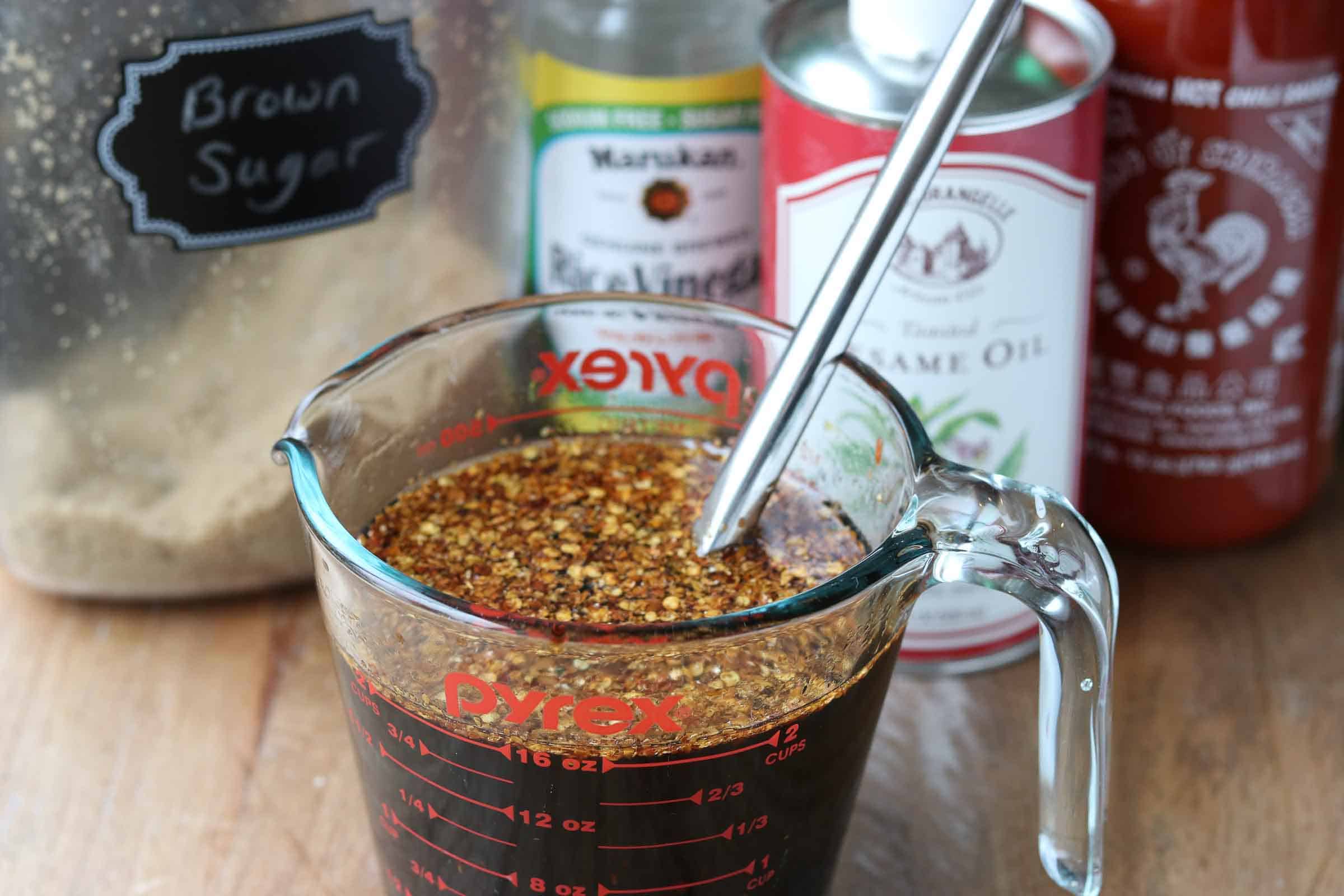 Glass measuring cup with sauce with brown sugar, rice vinegar, sesame oil, sriracha and red pepper flakes on a wooden board in the background from Gourmet Done Skinny