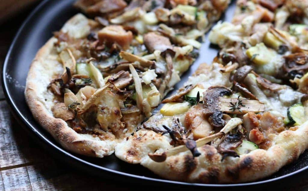 If you love mushrooms, this Healthy Wild Mushroom Pizza with Caramelized Onions, Garlic, Zucchini and Truffle Oil slices on a black plate from Gourmet Done Skinny