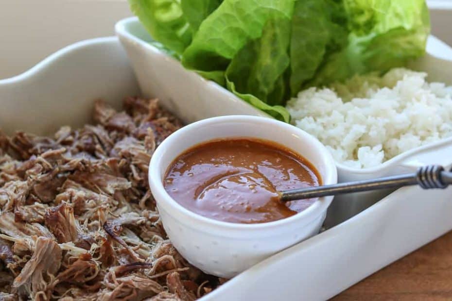 Kalua pork/kalua pig in a white dish with homemade hoisin sauce in a small white bowl with white rice and lettuce wraps on a wooden board from Gourmet Done Skinny