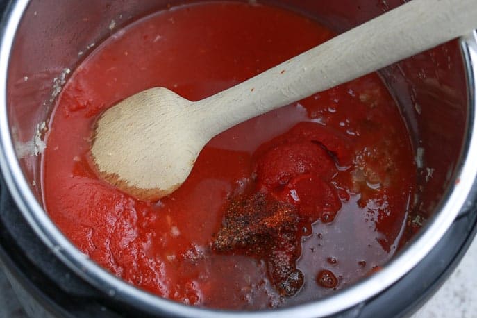 Tomato sauce, paste, spices, bourbon in an Instant Pot liner with a wooden spoon from Gourmet Done Skinny