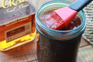 Blue Ball jar with homemade Instant Pot BBQ sauce, basting brush, bottle of bourbon on a wooden board from Gourmet Done Skinny