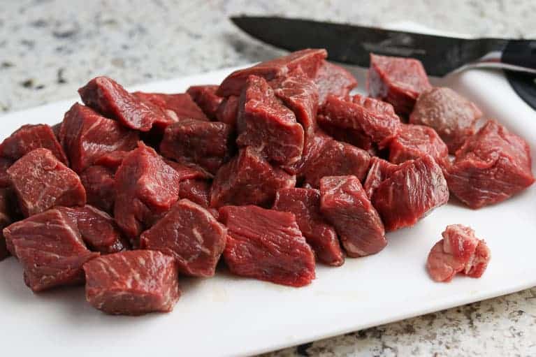 Beef cubes on a white cutting board on a granite counter top from Gourmet Done Skinny