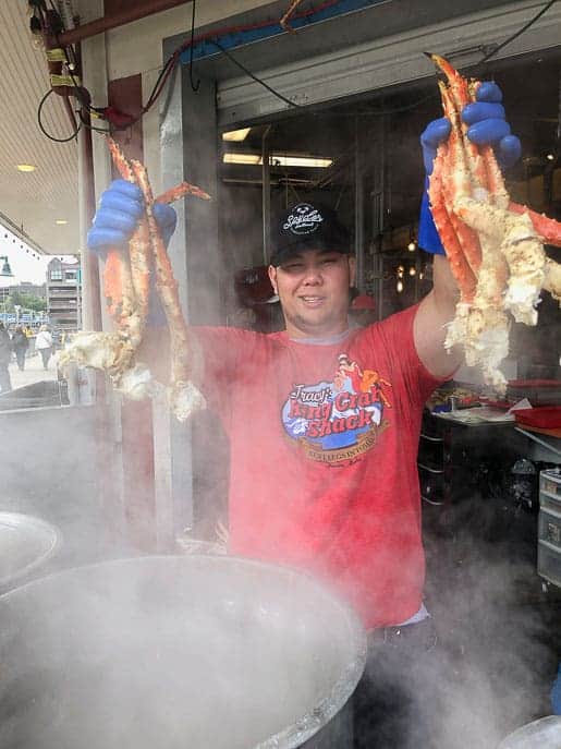 Man holding up crab legs over a pot of steaming water from Tracy's King Crab Shack