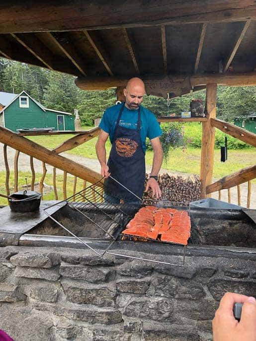 Man cooking salmon over a fire at Taku Lodge