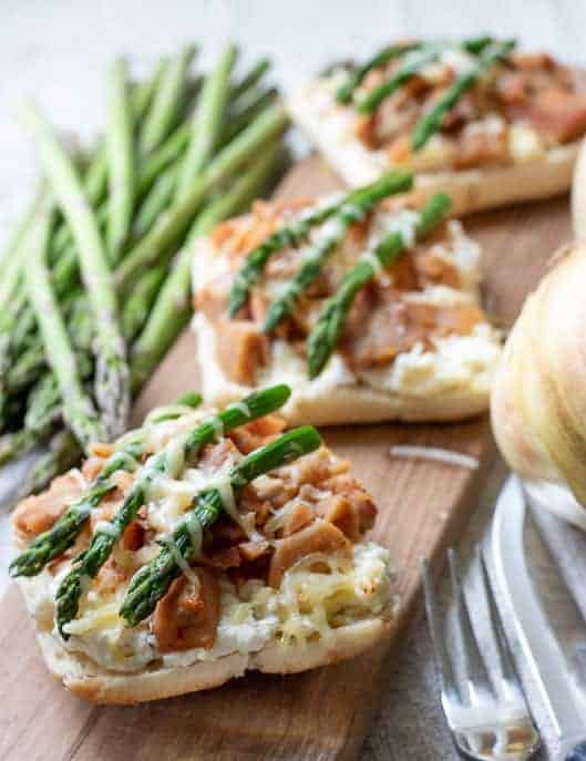 3 open faced Chicken Rainier sandwiches on a wooden board with asparagus, onion, fork and knife in background from Gourmet Done Skinny