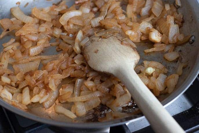 Walla Walla onions caramelizing in a skillet with a wooden spoon from Gourmet Done Skinny