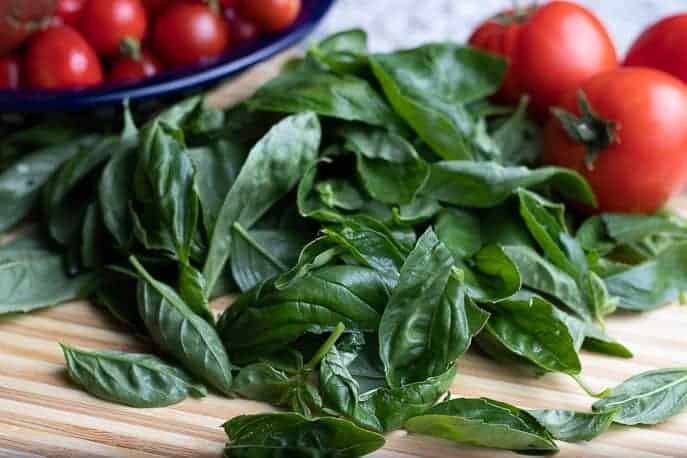 Fresh basil on a wooden cutting board with red tomatoes on the counter from Gourmet Done Skinny