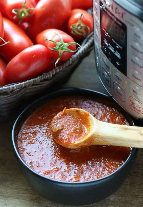 Instant Pot Roasted Tomato Sauce in a bowl with wooden spoon with Instant Pot and fresh tomatoes
