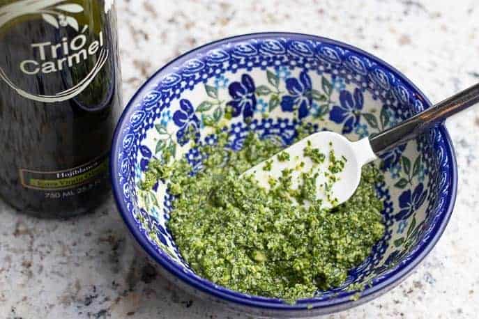 Blue Polish pottery bowl with homemade pesto, spatula and olive oil on a granite counter