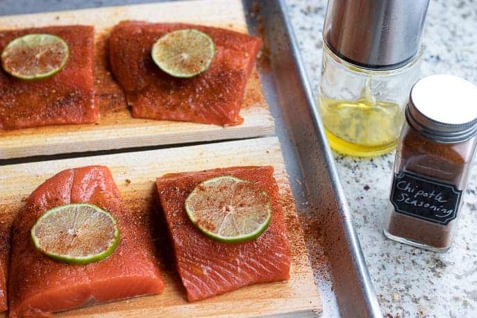 Salmon topped with Chipotle seasoning and lime on Cedar planks on a sheet pan with oil and seasoning from Gourmet Done Skinny