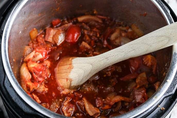 Tomato Bacon Jam mixture in the Instant Pot with a wooden spoon from Gourmet Done Skinny
