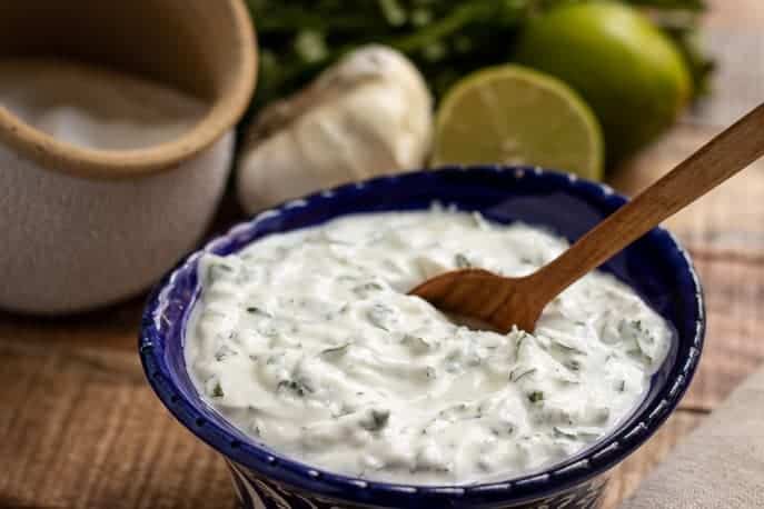 Cilantro Lime Yogurt Aioli in a blue bowl with salt, garlic, limes in background from Gourmet Done Skinny