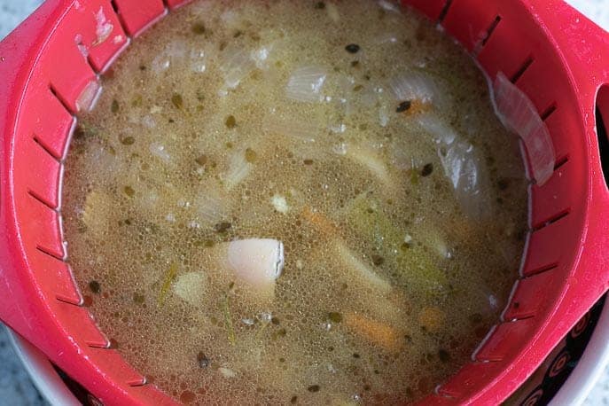 Parmesan chicken broth straining in a colander from Gourmet Done Skinny