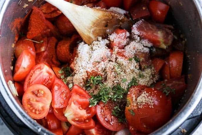 Tomatoes and remaining ingredients in the Instant Pot with a wooden spoon from Gourmet Done Skinny