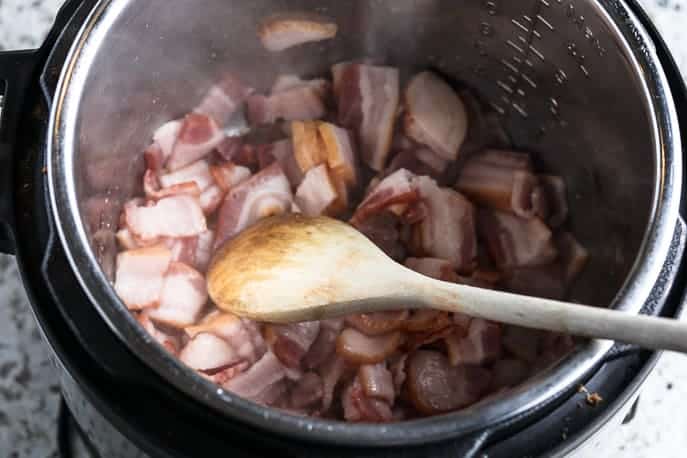 Bacon frying in the Instant Pot with a wooden spoon from Gourmet Done Skinny