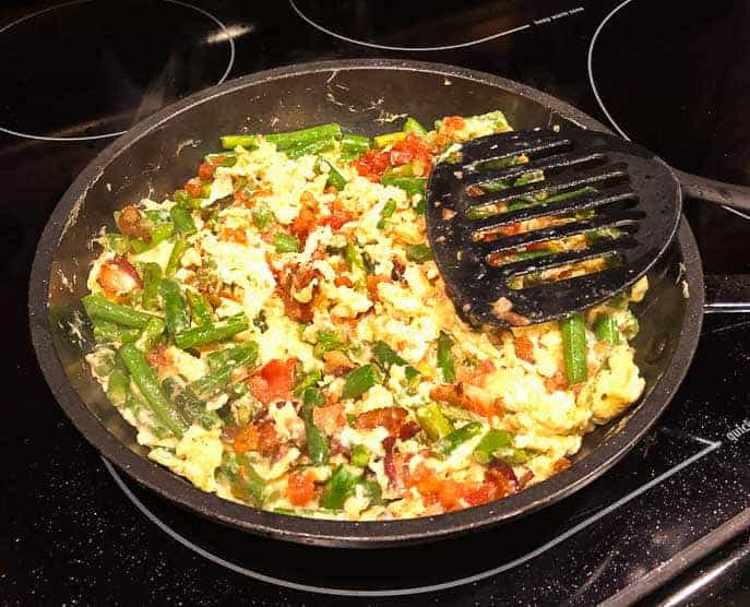 scrambled eggs and vegetables in a pan on the stove