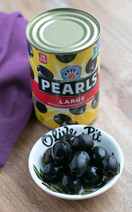 California Pearl black olives in a can with a dish of black olives on a wooden board from Gourmet Done Skinny