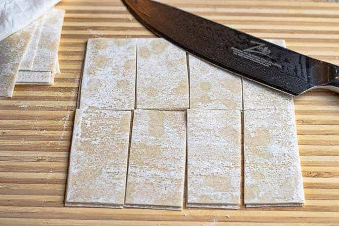 Egg roll wrappers on a cutting board cut into strips with a knife from Gourmet Done Skinny