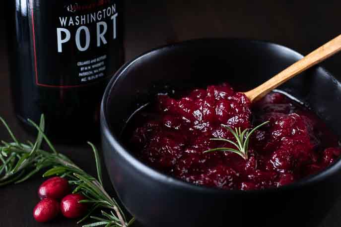 Cranberry sauce in a black bowl with a bottle of port, rosemary and cranberries from Gourmet Done Skinny