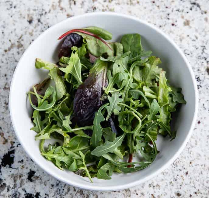 Greens in a white salad bowl on a granite counter