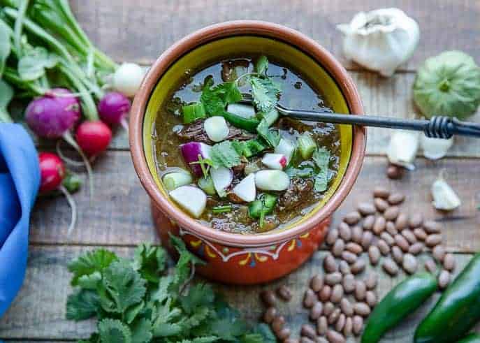 mexican soup with radishes, cilantro, green onion, beef in a bowl with spoon, beans, cilantro on a wooden board
