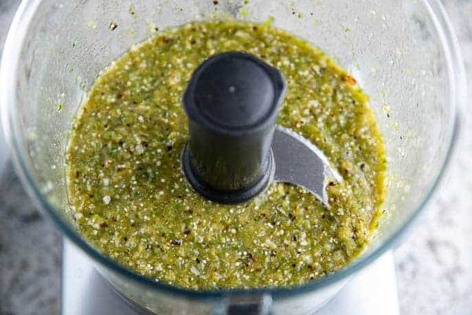 Food processor with blended tomatillos, peppers and garlic.